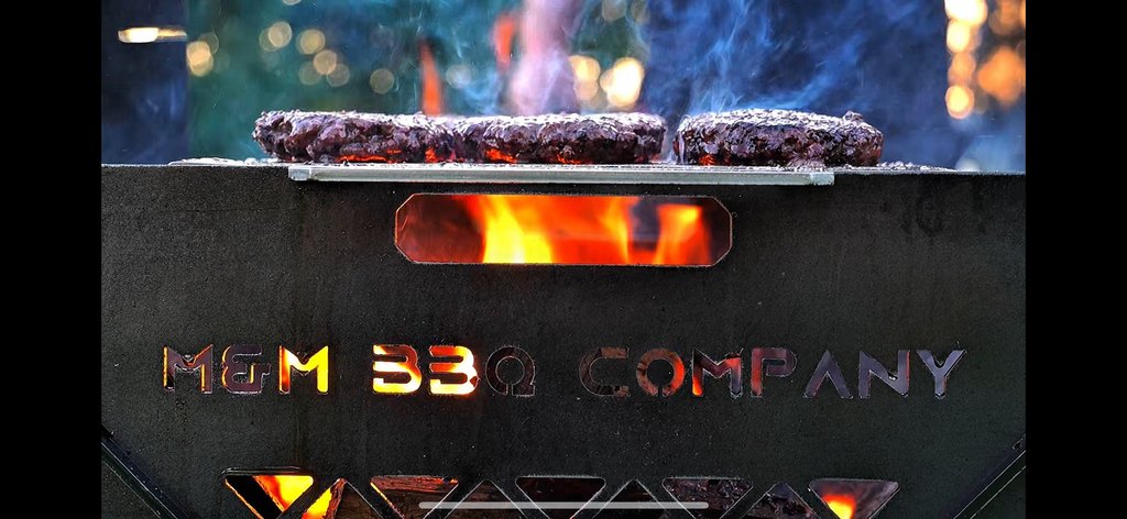 Burgers searing over the fire on a FireFly grill with the M&M BBQ Company cutout