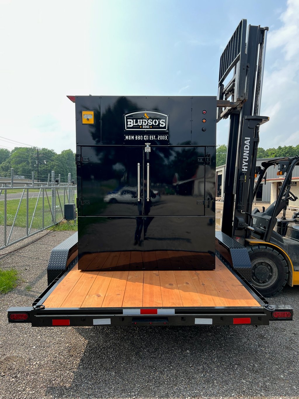 Black rotisserie smoker with Bludso's BBQ branding on a flatbed trailer